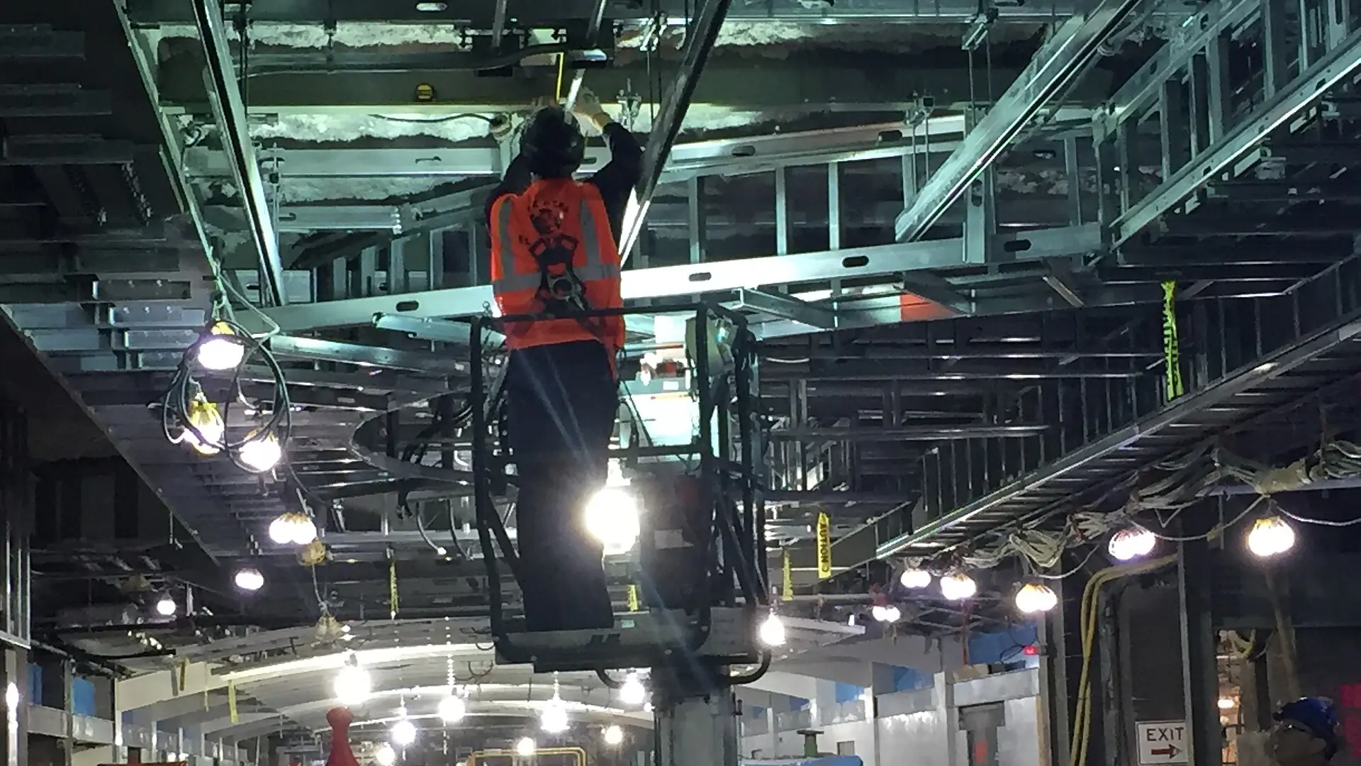 Electricians installing conduit overhead in a large construction corridor