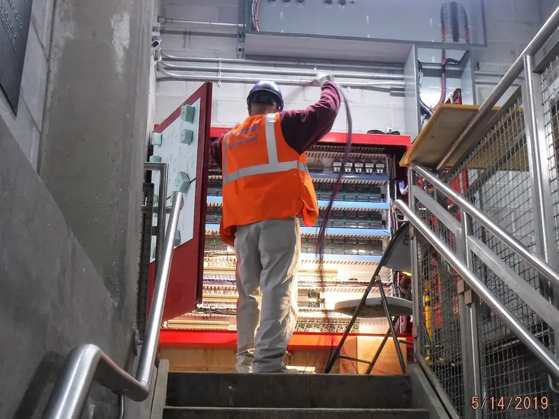An electrician working on a control panel at the top of a staircase