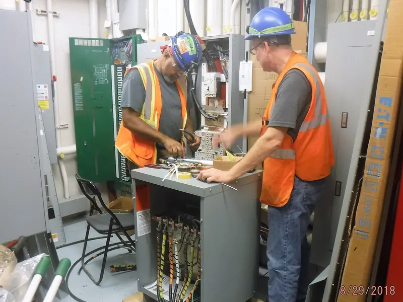 Two electricians in safety vests terminating wiring in an electrical cabinet